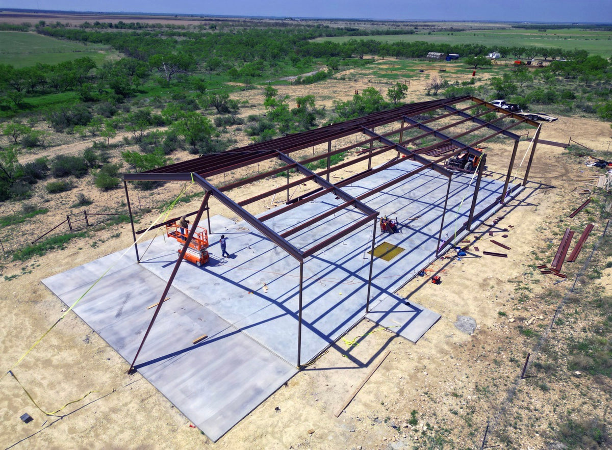 Aerial view of a red-iron steel building frame erected on a freshly poured concrete slab