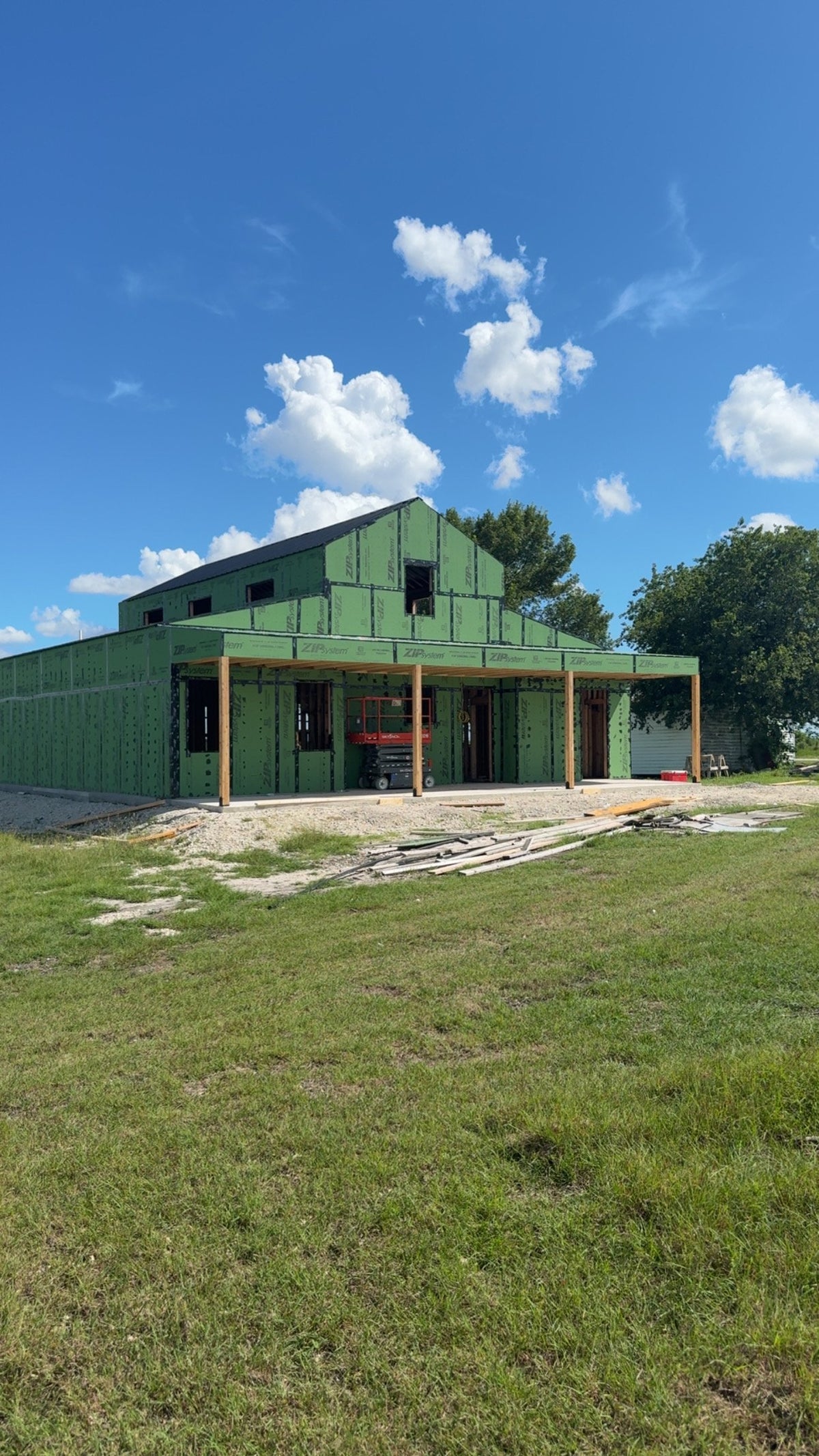 Barndominium with wraparound covered porch under construction, sheathed and dried in beneath a clear blue Texas sky