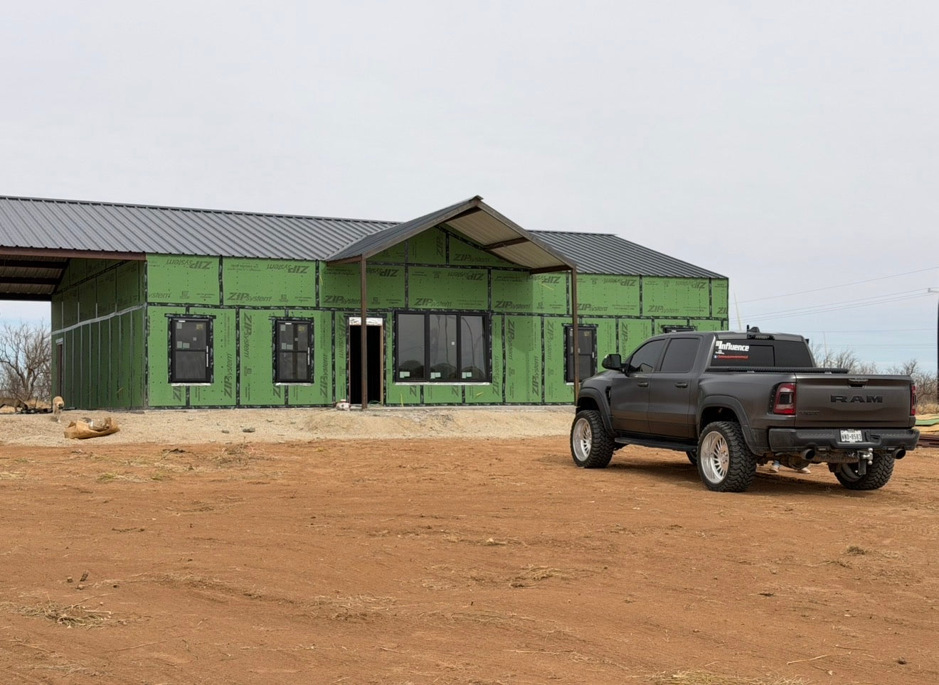 Barndominium under construction with green ZIP System sheathing, a dark metal roof, and a covered front porch