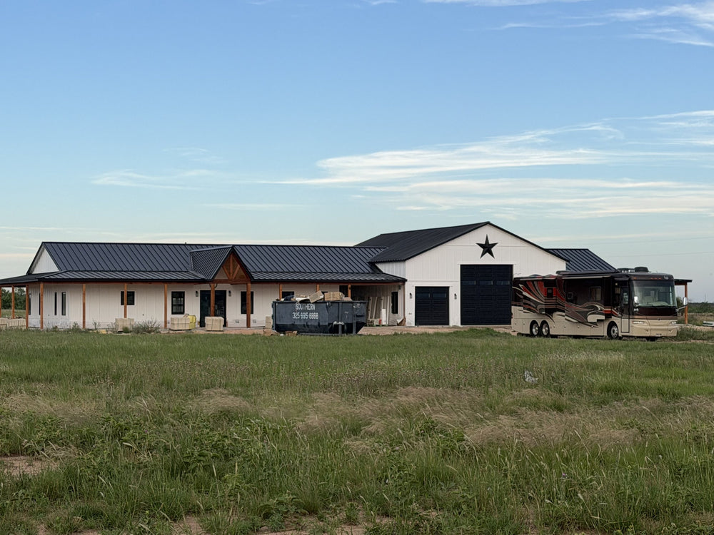 Finished white barndominium with black standing seam metal roof, Texas star gable, RV garage bay, and a covered wraparound porch