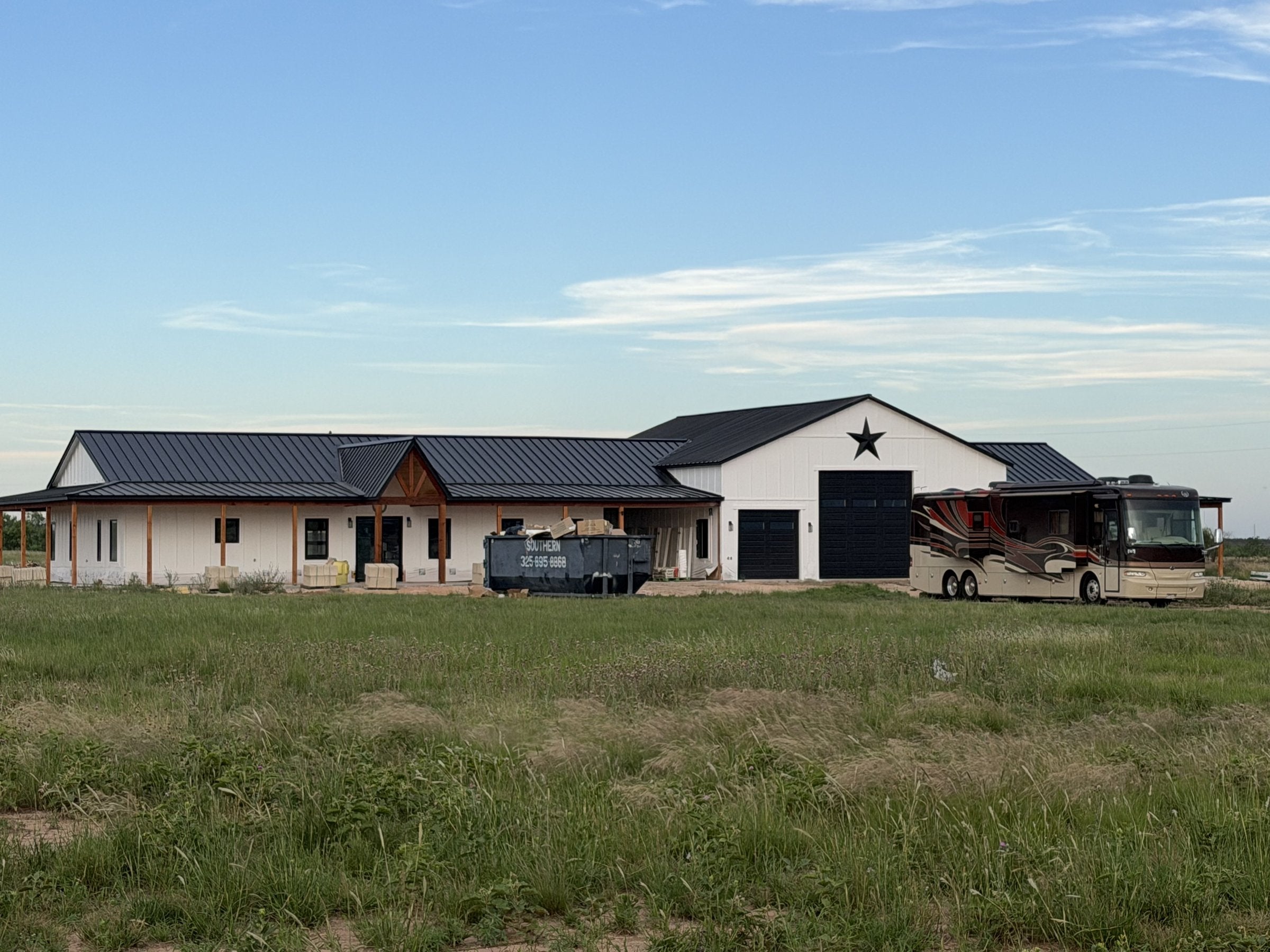 Finished white barndominium with black standing seam metal roof, Texas star gable, RV garage bay, and a covered wraparound porch