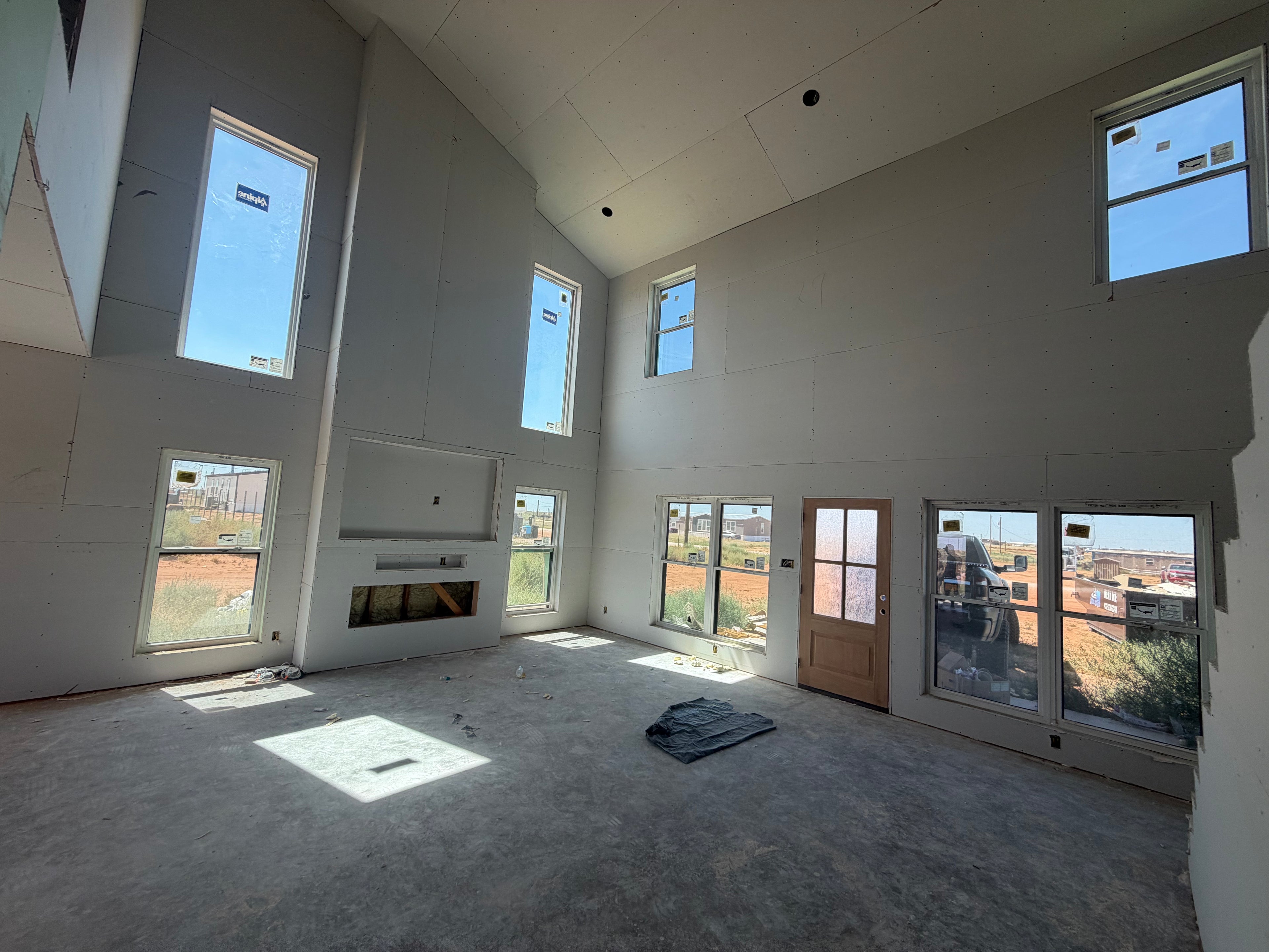 Custom home great room with drywall hung, a vaulted ceiling, tall windows, and a framed fireplace opening awaiting its stone surround