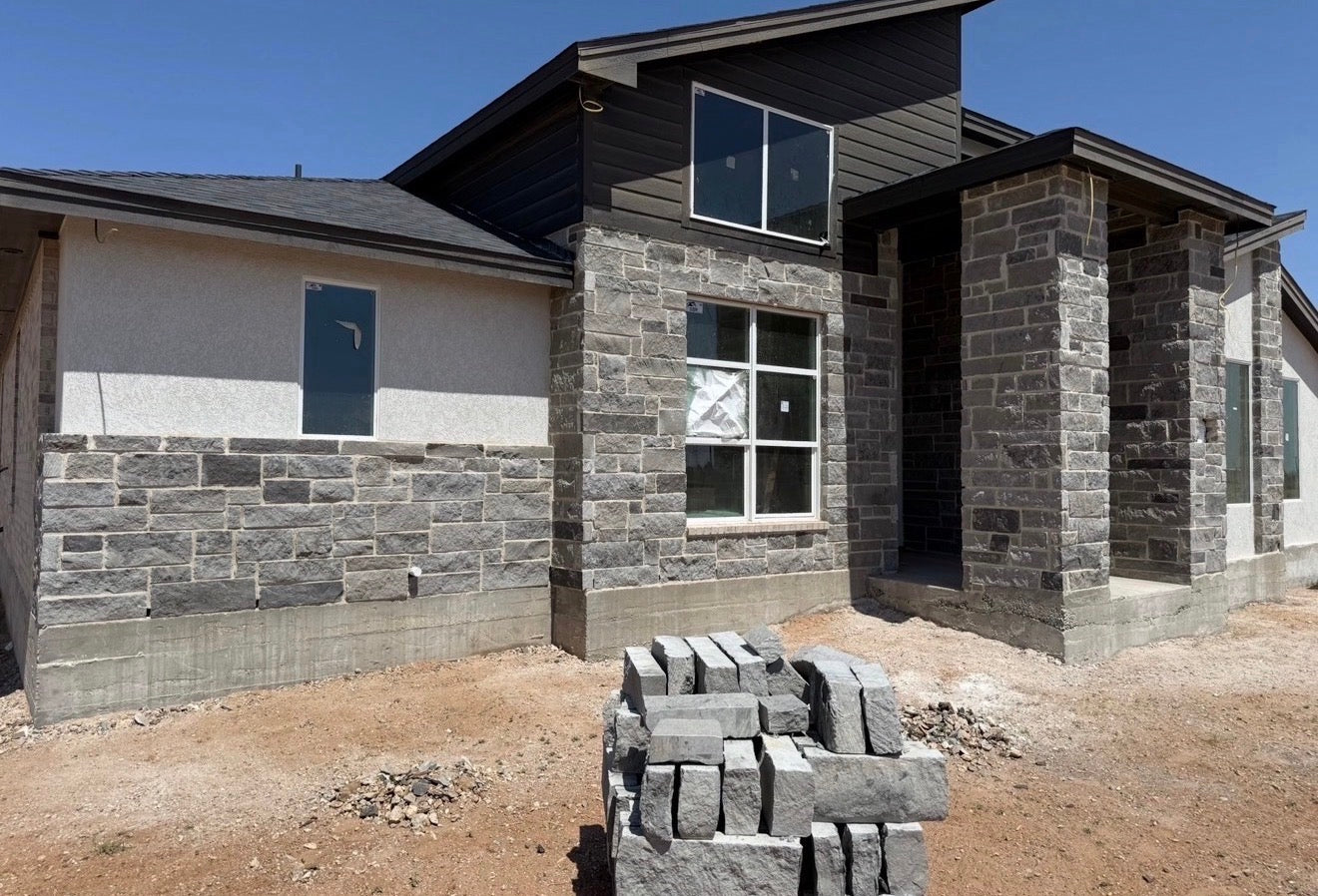 Custom home under construction with stone veneer being installed over the lower walls and dark board-and-batten siding above