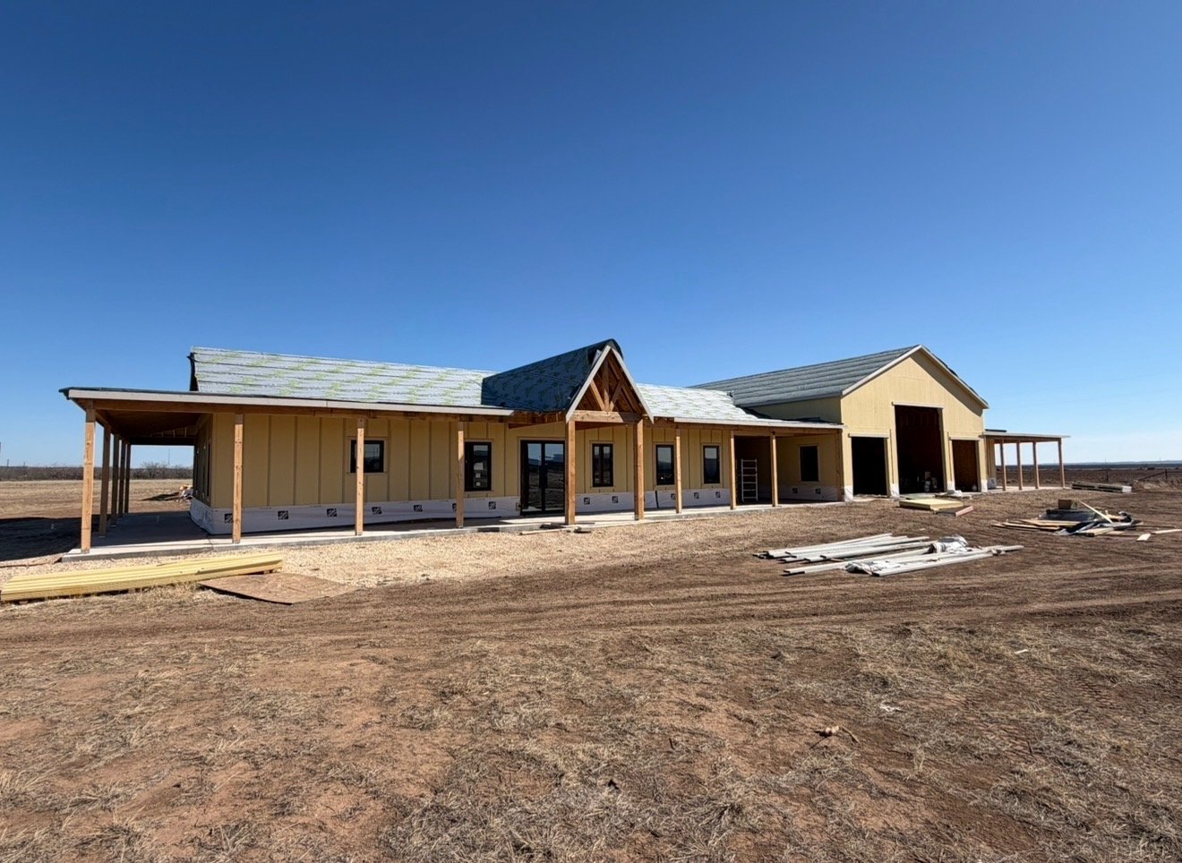Custom ranch-style home and attached shop framed, sheathed, and dried in with covered porches and a metal roof in West Texas