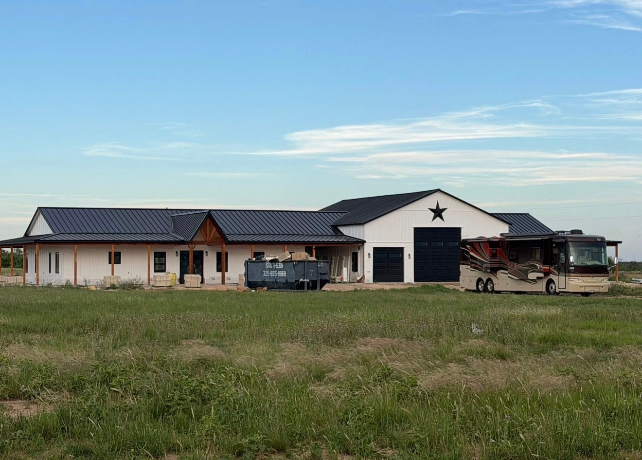Custom ranch home with a white and dark metal exterior and Texas star gable accent, under construction with an RV parked alongside