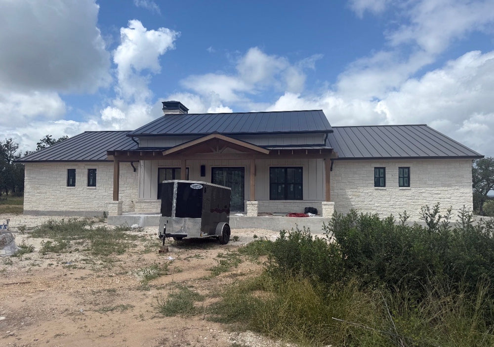 Single-story limestone ranch home with a dark standing seam metal roof and covered front porch, nearing completion