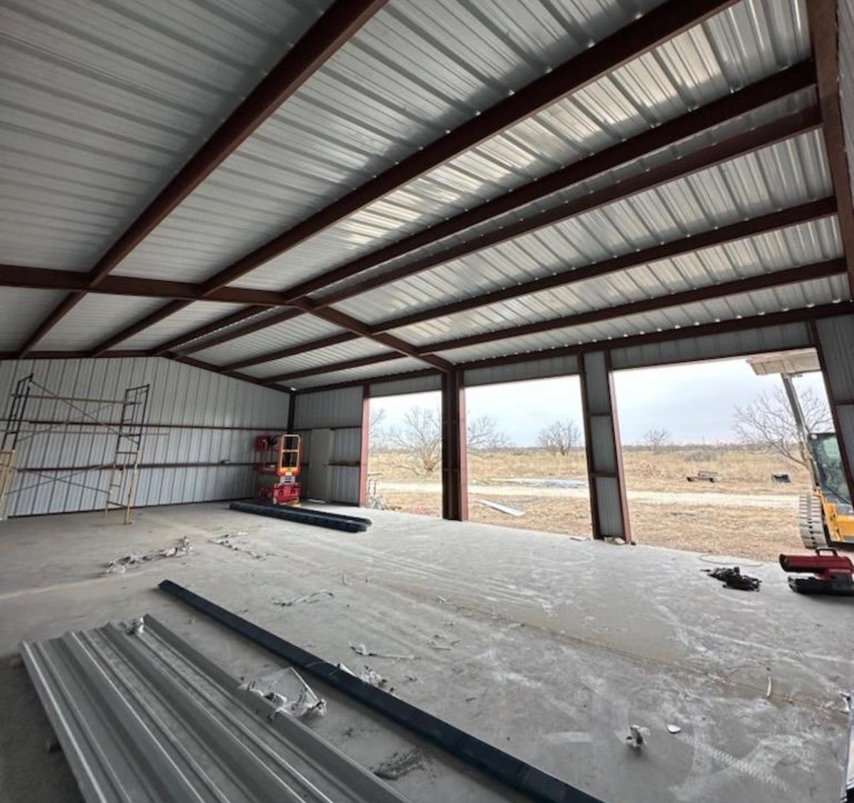 Interior of a metal building showing the red-iron frame, white liner panels, open bay doors, and a finished concrete slab