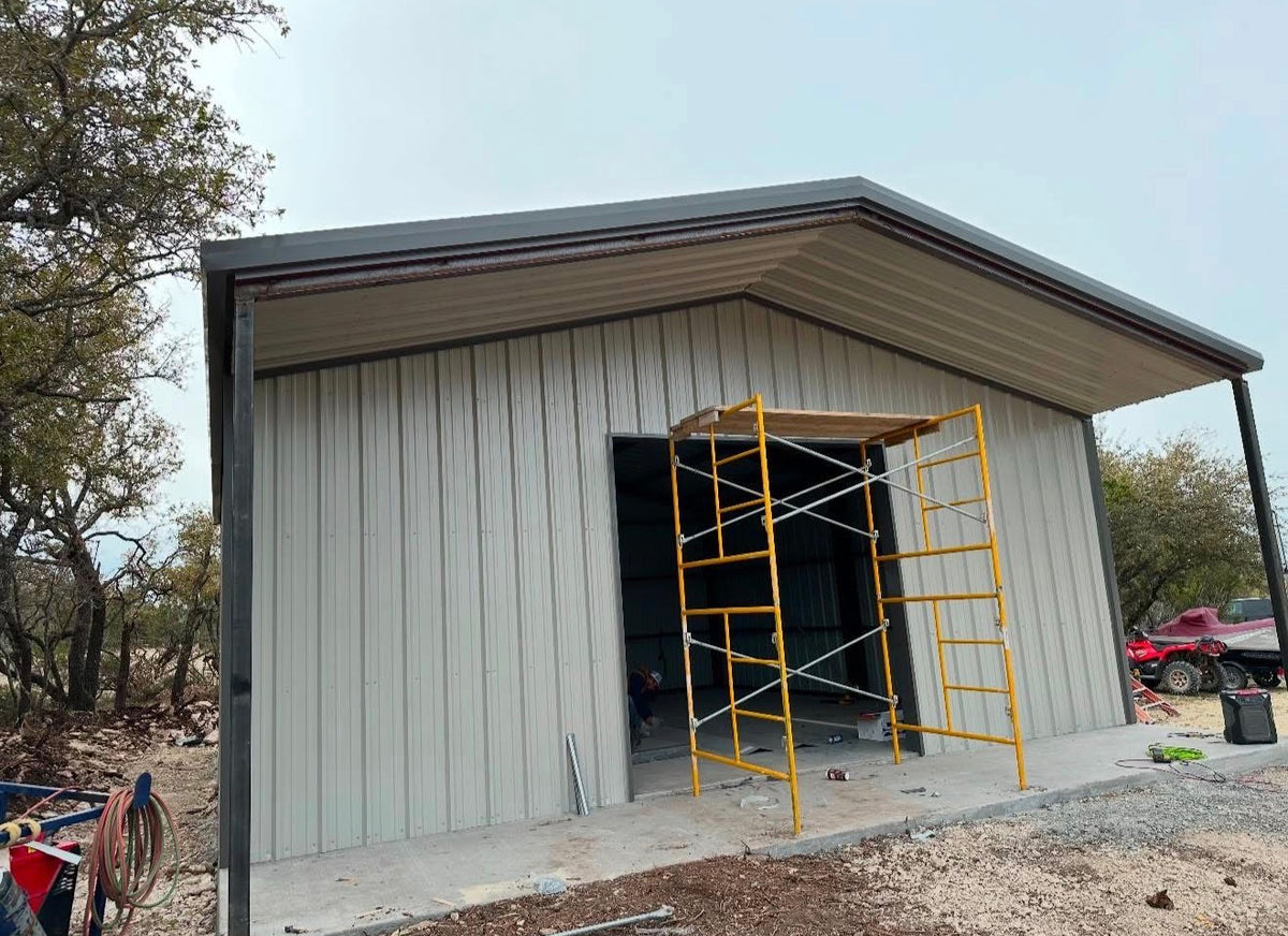 Cream metal building with a covered lean-to porch and yellow scaffolding set up at the entry during construction