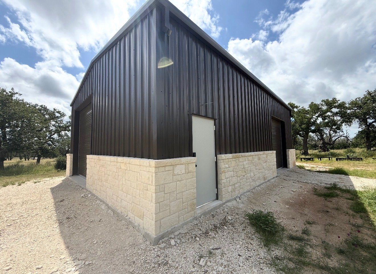 Dark bronze metal shop building with limestone wainscot and roll-up doors, built by Ironwood Builders in San Angelo, TX