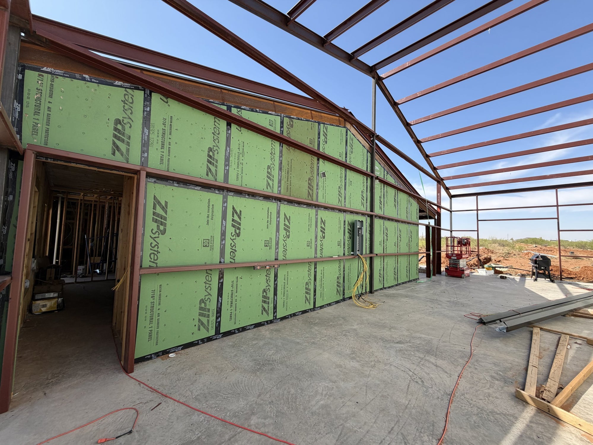 Interior of a metal building under construction showing red-iron steel framing, ZIP System sheathed walls, and a poured concrete slab