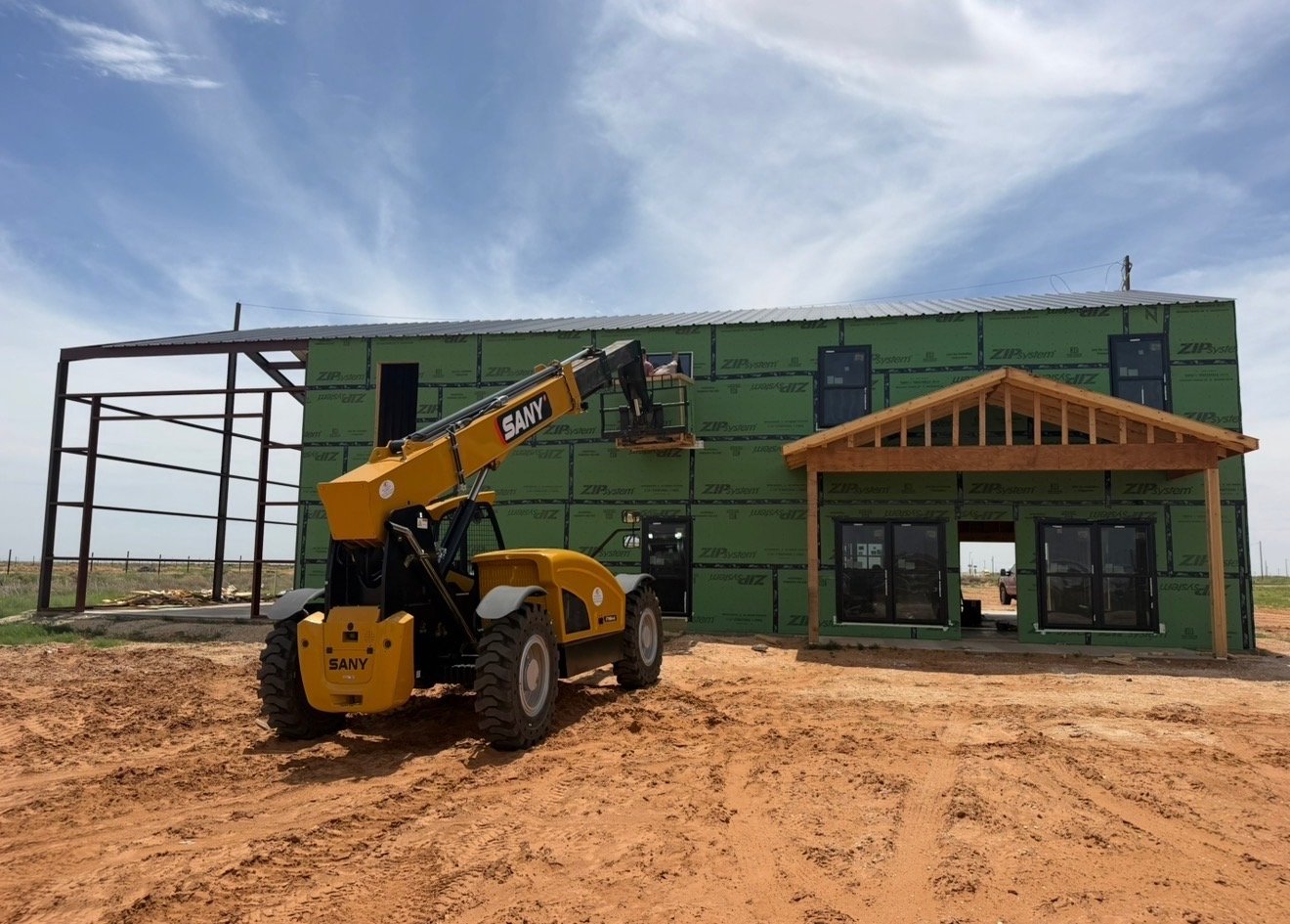 Telehandler lifting materials to the second story of a barndominium under construction on an Ironwood Builders job site