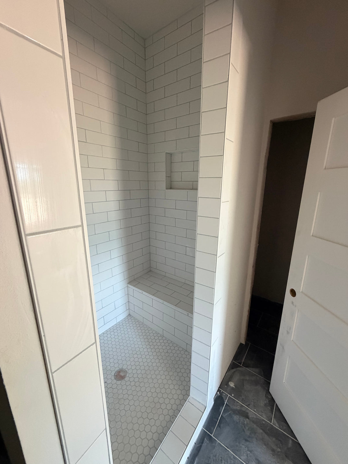 Finished walk-in shower with white subway tile, a built-in bench, recessed niche, and hexagonal mosaic floor tile