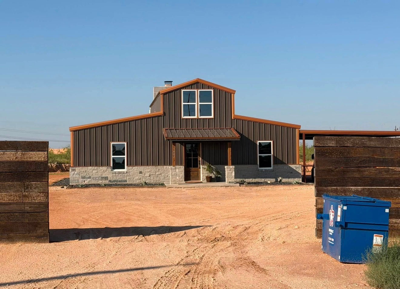 Completed two-story barndominium with bronze metal siding, a board-and-batten gable, stone base, and covered entry