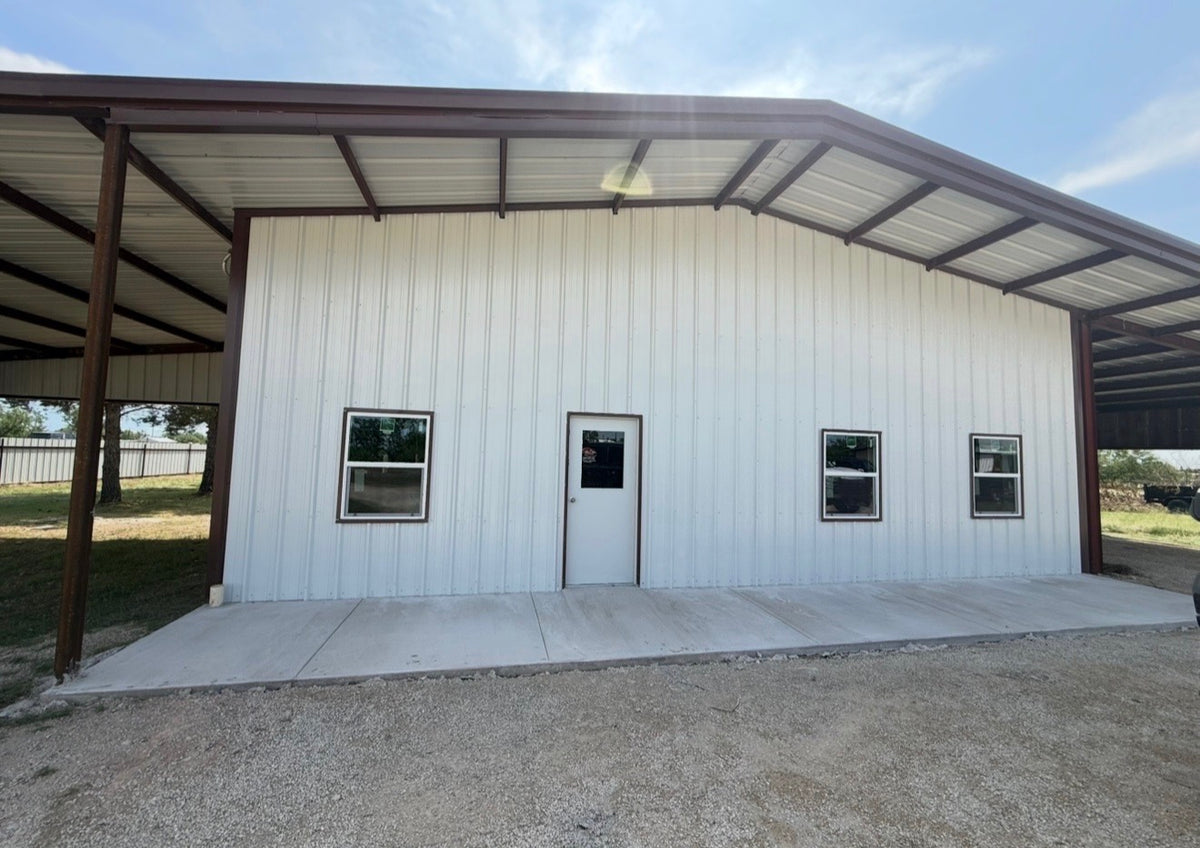 White metal barndominium with a covered lean-to porch, entry door, and poured concrete apron