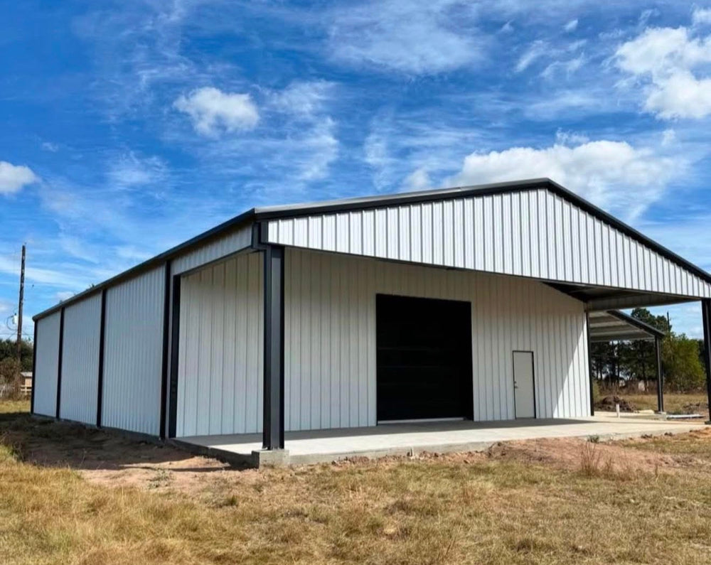 White metal shop building with black trim and a covered lean-to bay under a blue Texas sky